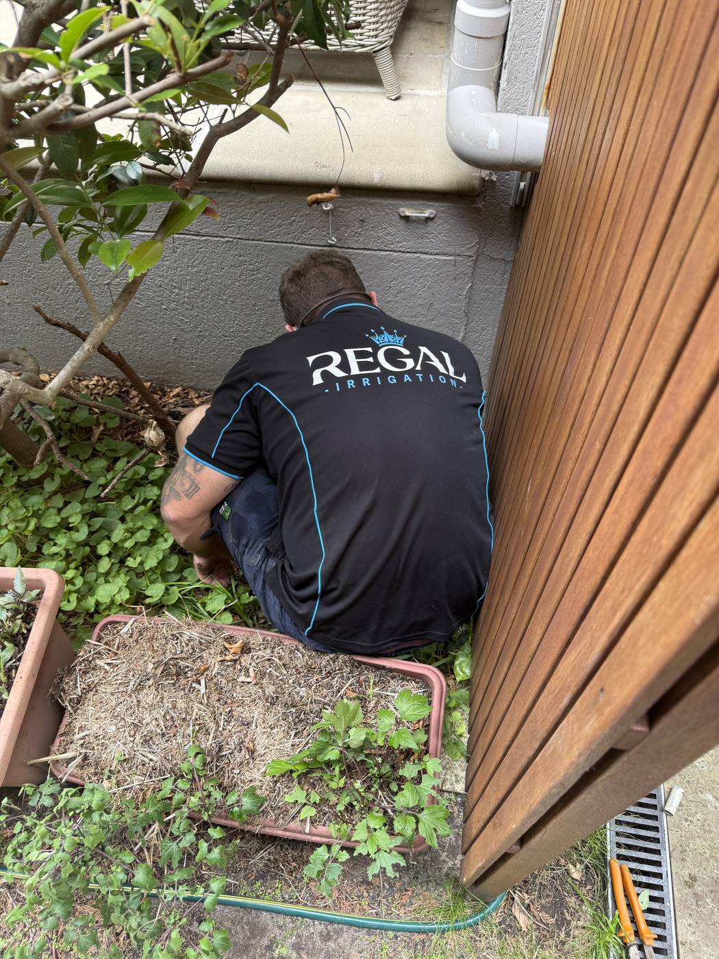 Working on a valve at the base of a fence, black uniform